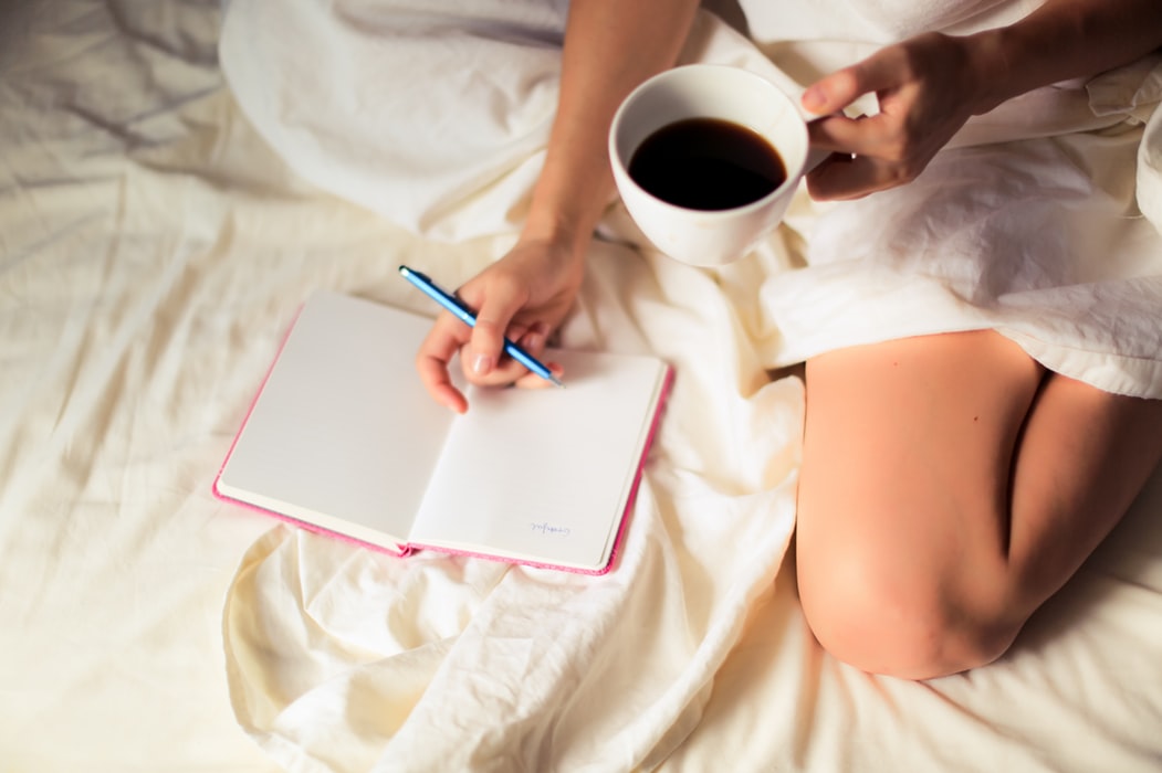 girl drinking coffee in bed writing notes